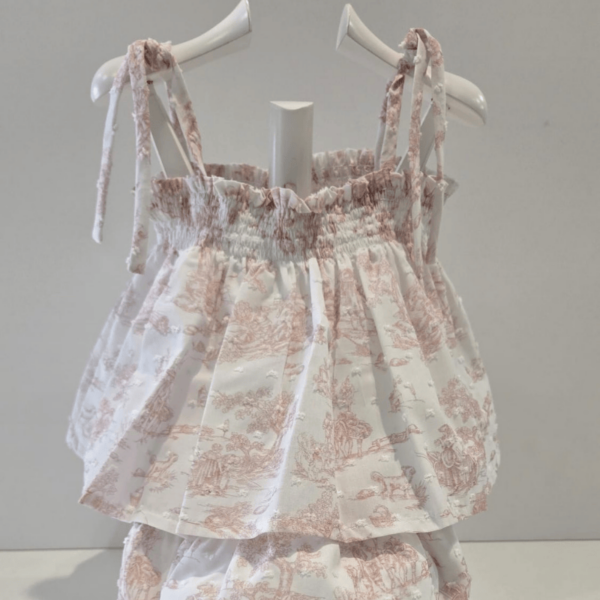 Este Jesusito se presenta con tirantes finos ideal para un look ligero y fresco. El cuerpo del top presenta un pequeño nido de abeja sobre tela rizada que proporciona elasticidad a la vez que decorativo. Los bordes de los bloomers están adornados con volantes que les da un aire juguetón. puedes apreciar un cuidado especial en los remallados y las terminaciones, se presentan ambas piezas en diseño toile de youy y es de la campaña primavera verano de la firma Martín Aranda.